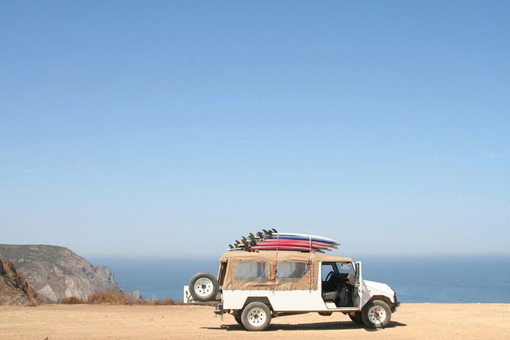 A jeep loaded with surfboards parked by a scenic ocean cliff under a clear sky.