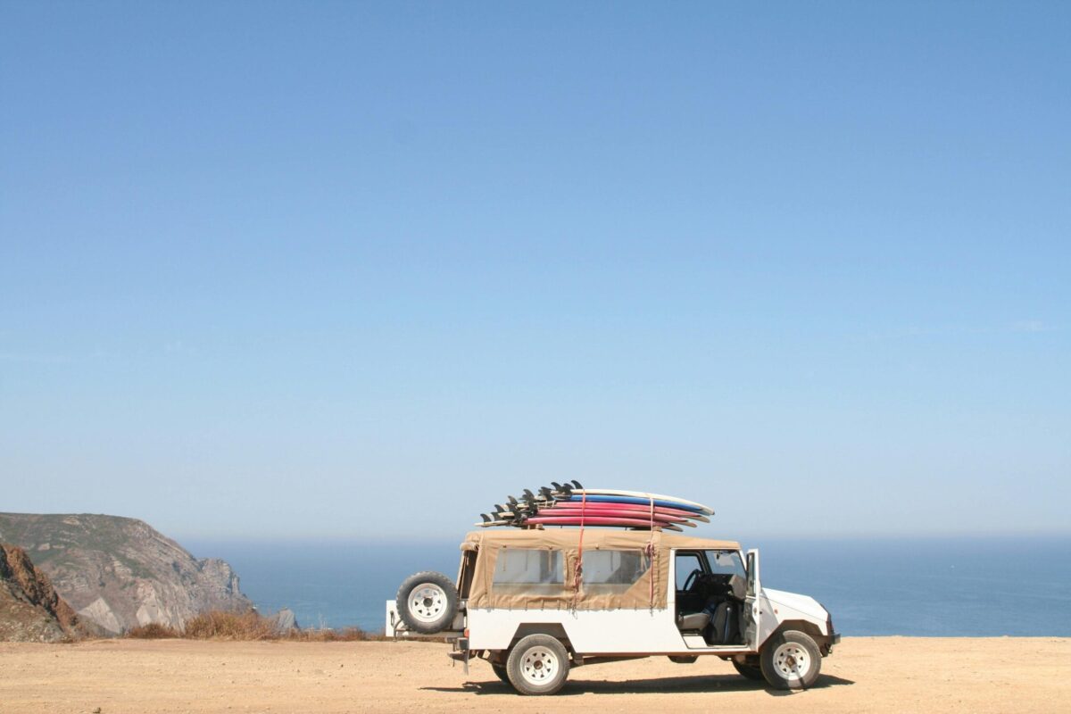 A jeep loaded with surfboards parked by a scenic ocean cliff under a clear sky.