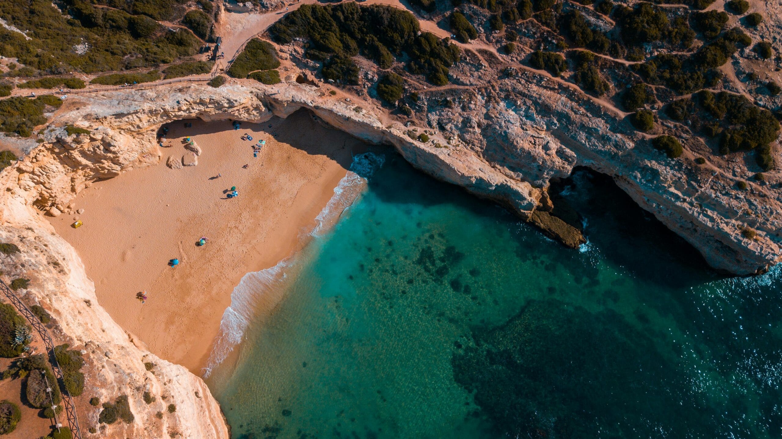 Stunning aerial shot of a secluded beach with golden sand and turquoise waters, surrounded by rocky cliffs.