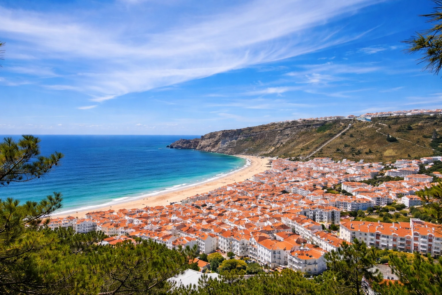 Panoramic view of Nazaré, Portugal from Sítio viewpoint showing red rooftops, cliff-lined coastline, and the Atlantic Ocean.