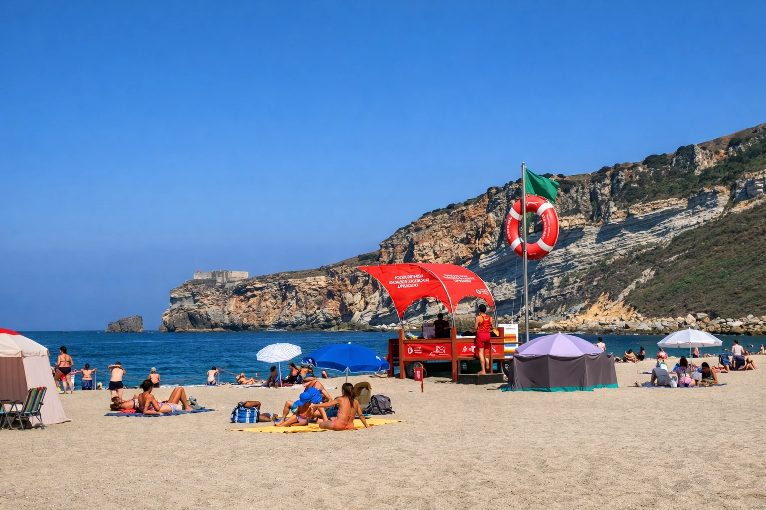 Lifeguard post on Praia da Nazaré with sunbathers on the sand and cliffs in the background on a clear summer day.